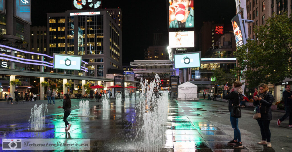 Yonge-Dundas Square fountain at night with coloured light jets and digital billboards, colourful Toronto street photography