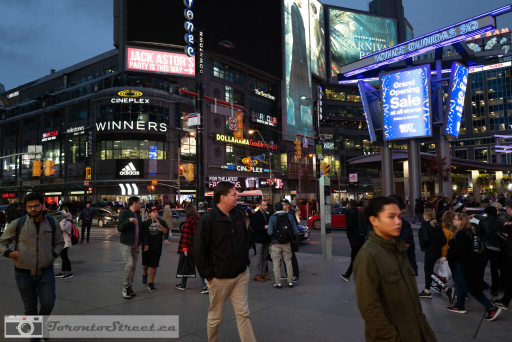 Yonge-Dundas Square at dusk, crowd moving below neon signs and billboards, colourful Toronto street photography