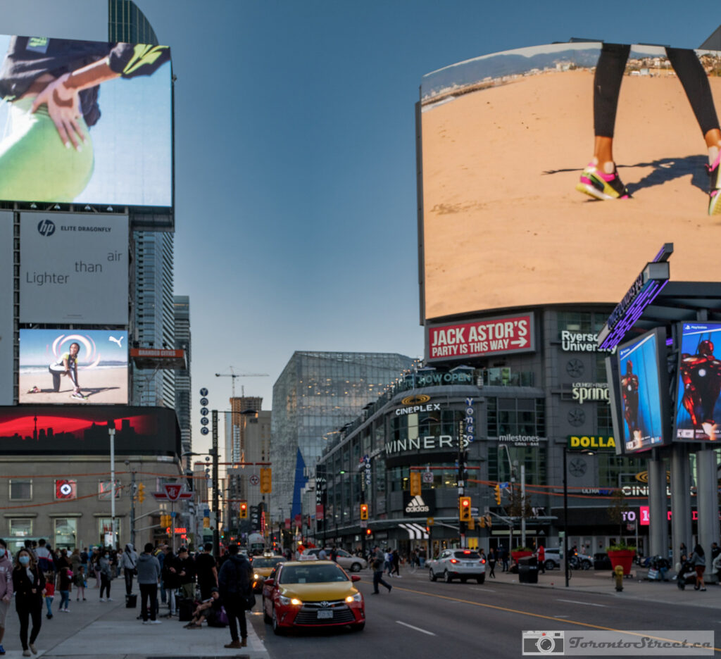 Yonge-Dundas Square daytime, massive digital billboards and yellow taxi