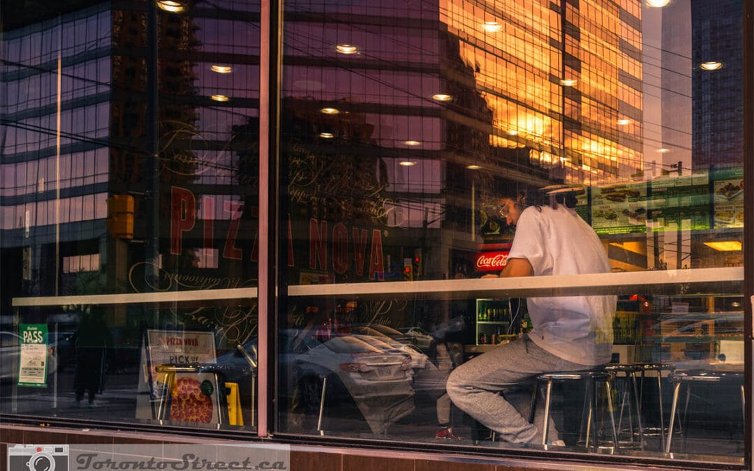 Toronto window street photography — man at diner counter with city sunset reflected in glass, Leica Q2