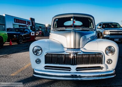 Head-on chrome grille of a white coupe with the Canadian Tire store behind at golden hour, Leica Q3