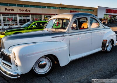 Side view of a low two-tone coupe parked by the Parts and Service doors, fender skirts, Leica Q3