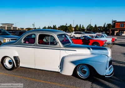1948 Mercury Eight coupe in profile, blue pinstripe and fender skirts, a row of classic cars behind, Leica Q3