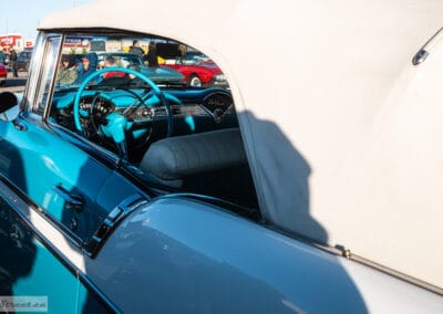 Turquoise steering wheel and dashboard seen over the door, the white folded top above, a red car reflected, Leica Q3