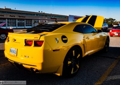 Rear three-quarter of a yellow 2012 Chevrolet Camaro RS with black stripes at a Richmond Hill cruise night, Leica Q3