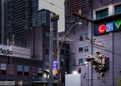 Stock-car sculpture bursting out of the CTV building wall above Queen. What a colourful city street photography opportunity for a Fuji X100V