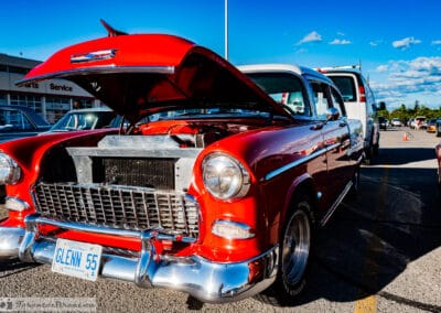 Red hardtop with the hood up showing the chrome engine, a white van behind in the lot, Leica Q3