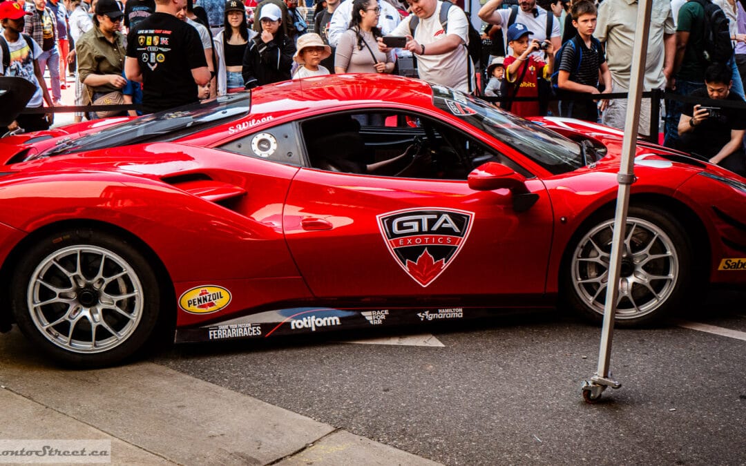 Crowd lifting phones around a red track car with a tall rear wing at the Yorkville car show, Leica Q3