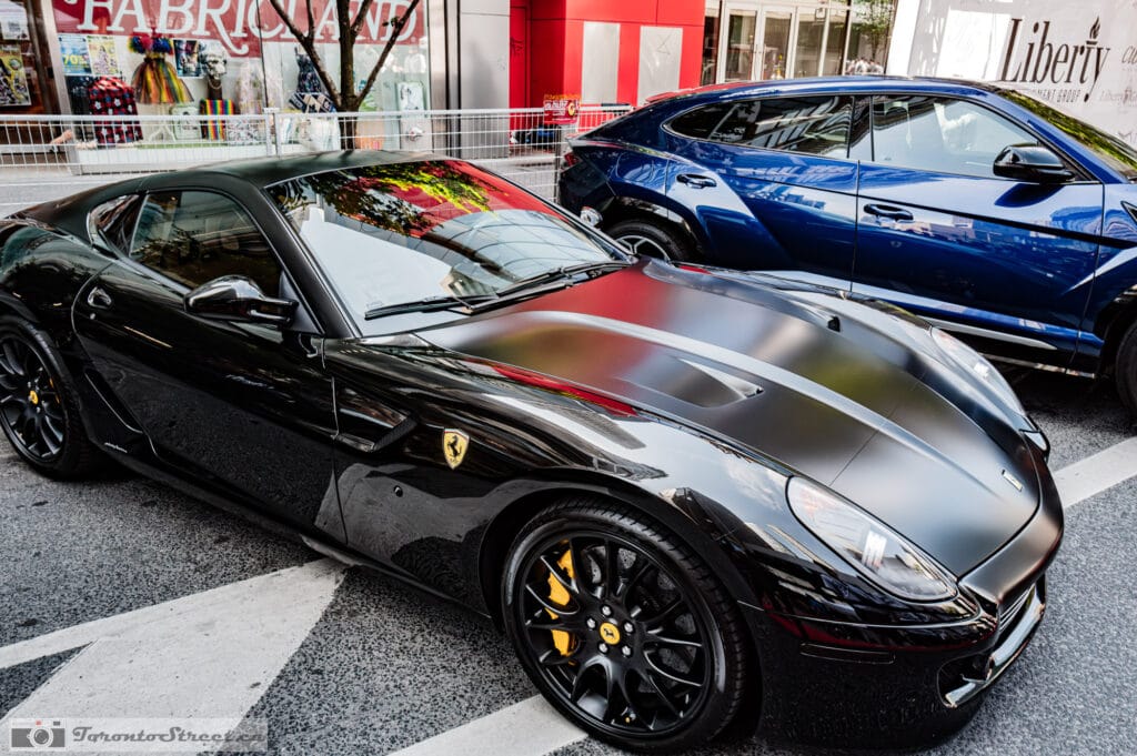 Ferrari 599 GTO--2 Glossy black coupe at a Yorkville curb, deep blue Lamborghini Urus behind, storefronts mirrored in the paint, Leica Q3