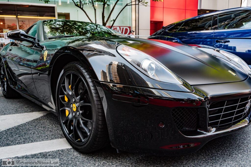 Ferrari 599 GTO--2-2 Low view of a black multi-spoke wheel and yellow brake caliper, glossy flank, blue Urus blurred behind, Leica Q3
