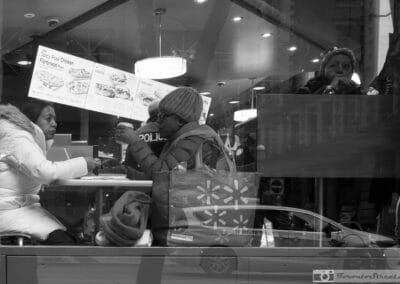 Black and white, a woman in a white puffer at a counter, a Walmart minivan ghosting across the glass, Leica Q3