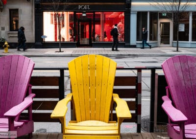 Two pink Muskoka chairs and a yellow one on a patio facing a red-lit POUT storefront, Toronto, Leica Q3