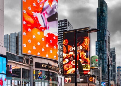Bright orange billboards under a dark storm sky at Yonge-Dundas, a woman in blue with a coffee, Leica Q3