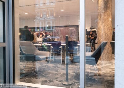 Toronto window reflections of a red-brick Victorian facade in a modern lounge, blue and grey chairs inside, Leica Q3