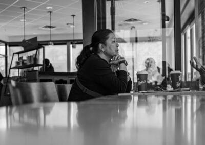 Black and white, two women in animated conversation at a coffee shop table, hands gesturing over their cups, Leica Q3