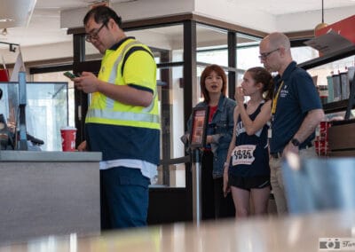 Woman with race bib 1935 in line at the coffee counter beside a construction worker in a hi-vis vest, Leica Q3