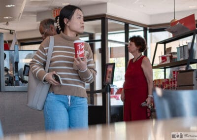 Young woman in a striped sweater holding a Tim Hortons cup, a woman in a red dress behind her, Leica Q3