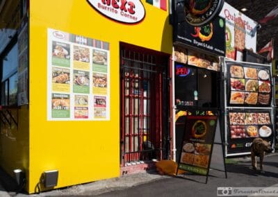 Bold yellow Next Burrito Corner storefront on a sunny Toronto street, a dog walking past, midday light, Leica Q2