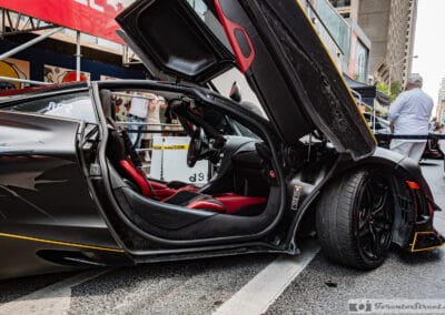 Open dihedral door revealing red and charcoal seats and a gold-caliper wheel, Leica Q3