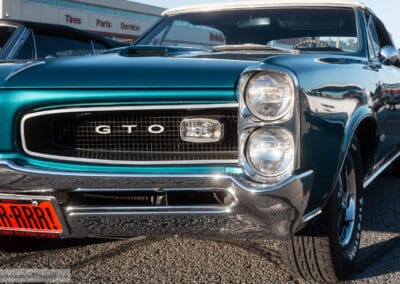 Stacked headlights and the GTO grille badge on a turquoise muscle car in low evening sun, Leica Q3