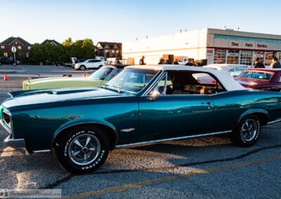 Turquoise convertible in profile, white top up, suburban plaza and houses in golden-hour light, Leica Q3