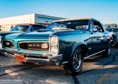 Turquoise drop-top catching the last low sun across a parking-lot car meet, Leica Q3