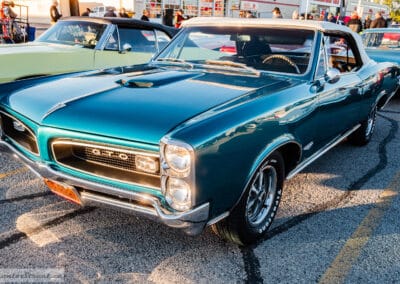 Pontiac GTO in a row of classic cars at the Monday-night meet, people browsing behind, Leica Q3
