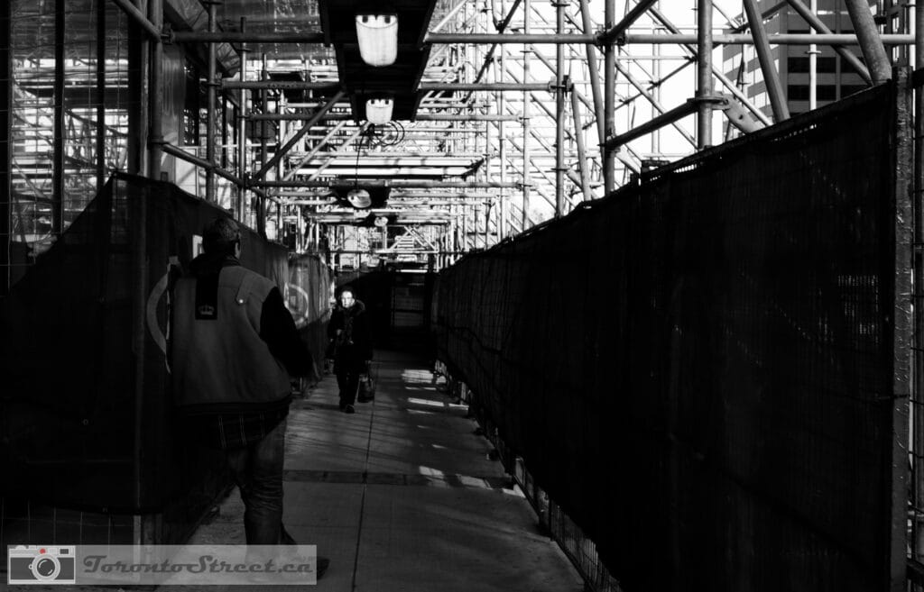 Street_Nov23_2019-1000933 Lone figure lit by single work lamp in dark Toronto construction corridor, black and white street photography, Leica Q2