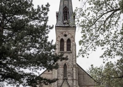 Stone church with a tall spire under an overcast sky, quiet neighbourhood sidewalk, Fuji X100V