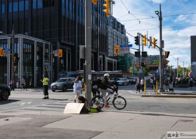 Person with a cardboard sign at a downtown intersection, a cyclist stopped nearby on a quiet afternoon, Fuji X100V