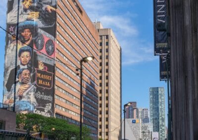 Massey Hall mural on a downtown building, pedestrians passing below on a warm afternoon, Fuji X100V