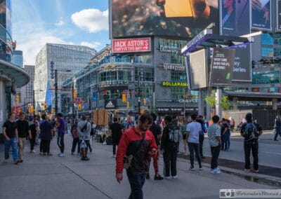 Man in a red jacket absorbed in his phone at Yonge-Dundas Square, digital billboards above, toronto sunday street photography, Fuji X100V