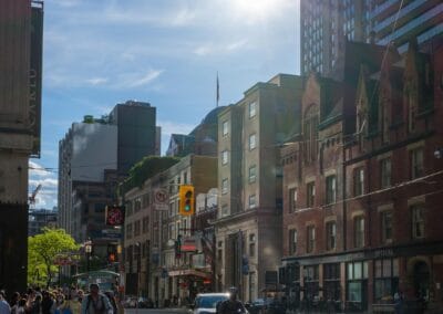 Toronto sunny day street photography, downtown street with a large sun flare over cyclists and warm brick buildings, Fuji X100V