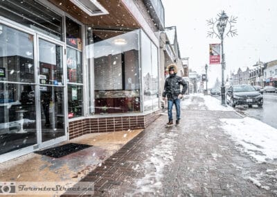 Man walking alone on a snowy Yonge Street in Richmond Hill, dark storefronts behind him, yonge street photography, Leica Q2