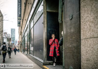 Woman in a bold red plaid coat in a recessed doorway on Yonge Street, toronto street photography interesting people, Leica Q2