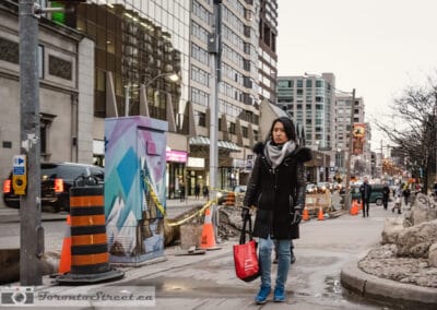 Woman in a black coat with a grey scarf and red bag walking past a construction zone, Leica Q2