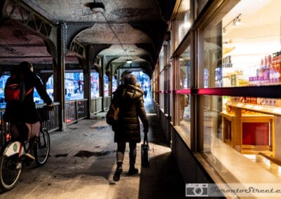 Woman and a cyclist moving through the railway underpass near St. Clair, warm shop light, Leica Q2
