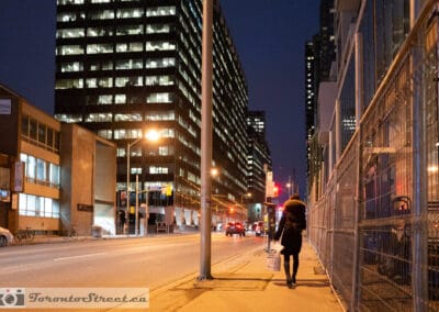 Lone figure with a backpack on Yonge Street at night, construction fencing and lit office towers, yonge street photography, Leica Q2
