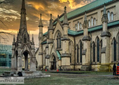 St. James Cathedral at dramatic sunset, gothic spires lit in orange, a woman in a colourful striped outfit in the foreground, Leica Q2