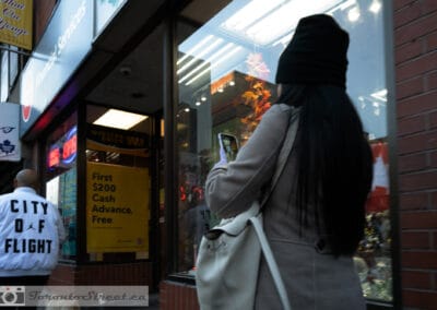 Woman shooting a store window along Yonge, a man in a City of Flight jacket behind her, Leica Q2