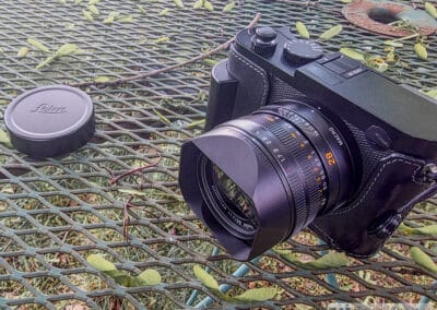 Leica Q3 with black tape over the top microphone holes, 28mm Summilux lens and hood, lens cap beside it, Galaxy Z Fold7