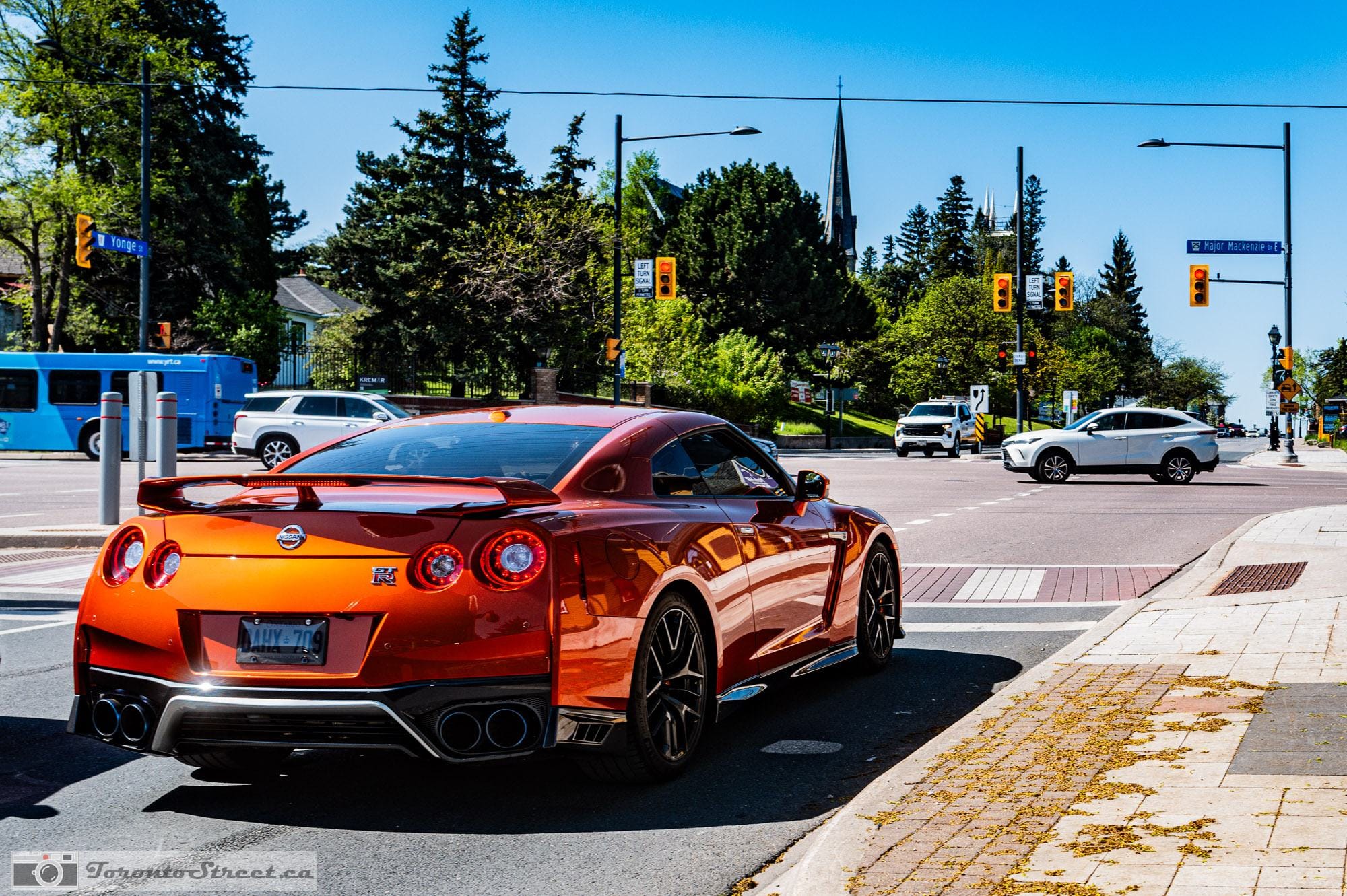 Orange Nissan GT-R stopped at a red light on a downtown Toronto corner, a church spire and city traffic behind it, shot on the Leica Q3. The grab shot that first put cars on the site.