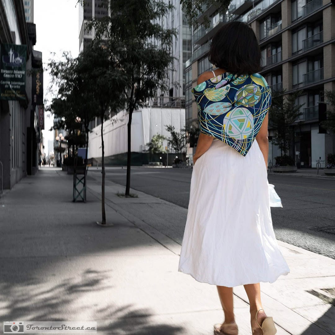 One Bright Shawl on an Empty Block Woman in a long white skirt and a blue and green patterned shawl walking away down an empty downtown sidewalk in late golden light, Toronto, Leica Q2