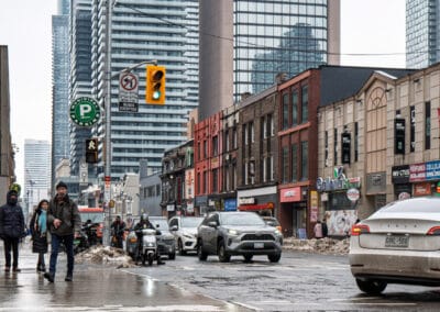 Toronto winter street photography at Yonge and Wellesley, people crossing grey slush under the towers, Leica Q3