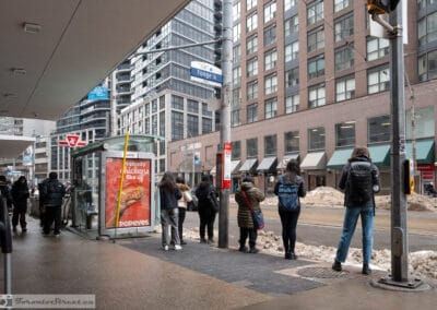 People waiting at a Yonge transit stop in the cold, snowbanks and a Popeyes ad behind them, Leica Q3