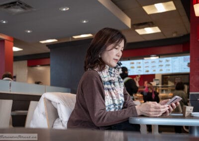 Woman in a cozy sweater checking her phone at a Tim Hortons table, tim hortons street photography, Leica Q3