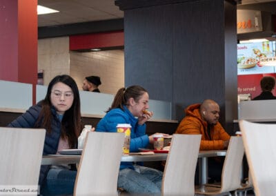 Three customers at separate tables, one studying, one eating, one listening to music, Leica Q3