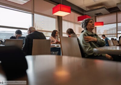 Woman in a headscarf seated beneath bold red pendant lamps, the warm glow of the room behind her, Leica Q3