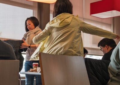Woman helping a friend put on a jacket by the door, warm red lamps and frosted windows behind, Leica Q3