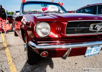 Close view of a headlight, chrome bumper and grille corral, a passerby in plaid trousers, Leica Q3